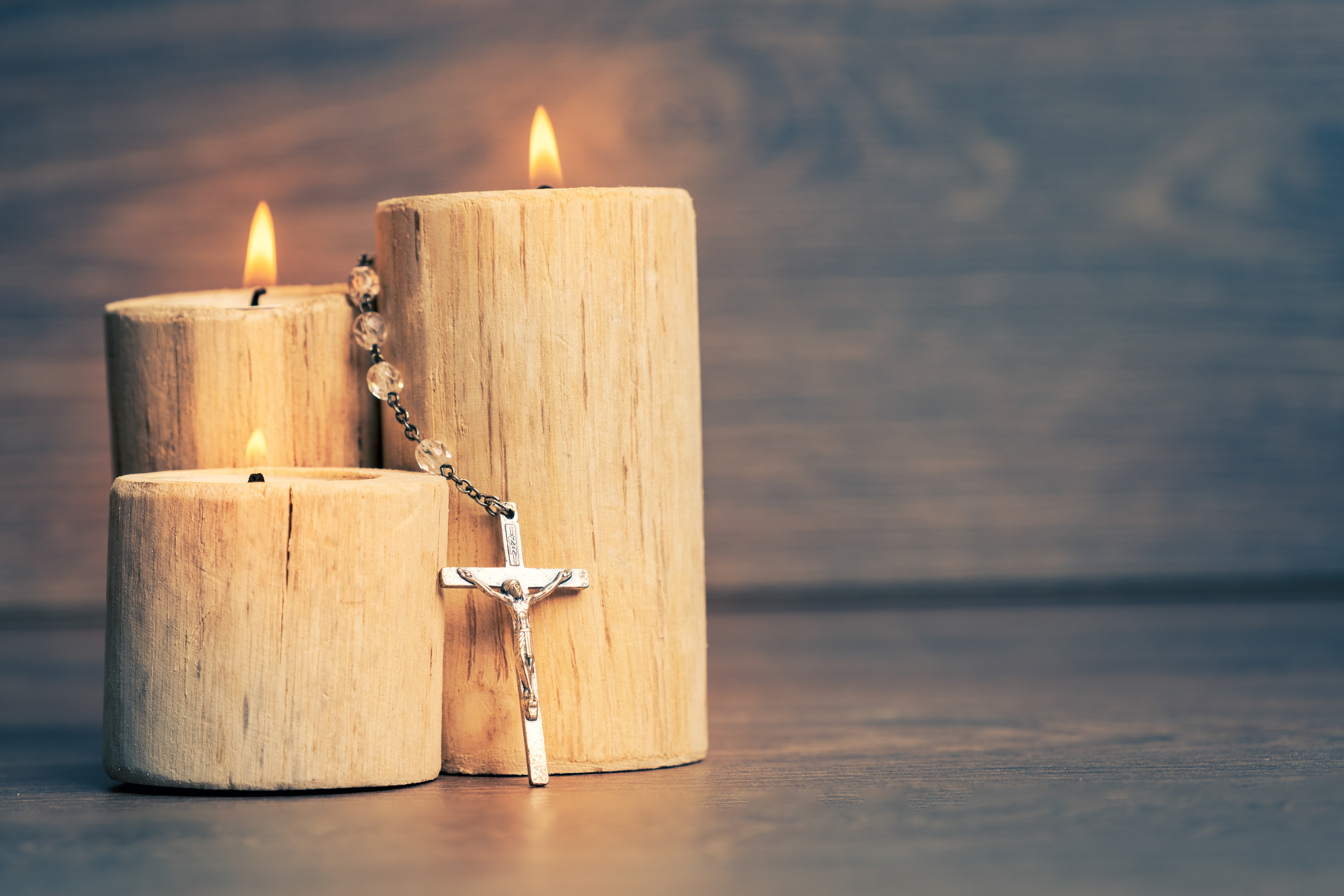 Silver rosary with Jesus on the Candle at wooden table,religion concept,vintage style with split toning.